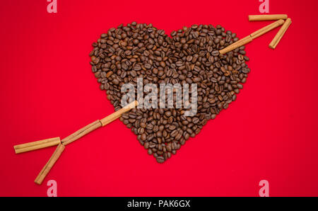 Coffee love suggested by a heart made from coffee beans and an arrow made from cinnamon sticks on a red romantic background Stock Photo