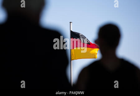 Warendorf, Germany. 24th July, 2018. The silhouettes of mourners can be seen in front of a German flag at the memorial service for Hans Guenter Winkler. Winkler had died in Warendorf on 9 July 2018. Credit: Friso Gentsch/dpa/Alamy Live News Stock Photo