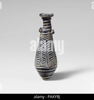 Glass alabastron (perfume bottle). Culture: Greek, Eastern Mediterranean. Dimensions: Height: 4 1/2 in. (11.5 cm)  Diameter: 1 1/2 × 7/8 in. (3.8 × 2.3 cm). Date: 2nd-mid-1st century B.C..  Translucent blue, with handles in same color; trails in opaque white.  Rim-disk with thick rounded edge, uneven and sloping inward, with projecting jagged inner edge to neck; slender cylindrical neck, slanting to one side; straight-sided fusiform body expanding downward, then tapering in to pointed bottom; two large horizontal lug handles applied over trail at top of body.  Trail wound unevenly around edge  Stock Photo
