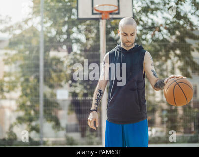 Bald attractive man playing basketball on the basketball court. Man is on focus and foreground, background is blurred.