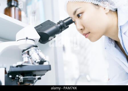 Portrait of young Asian woman  looking in microscope while doing research in medical laboratory Stock Photo