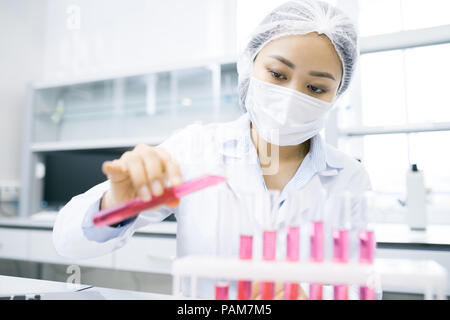 Portrait of Asian female scientist working on research studying liquids in beakers while sitting at table in laboratory Stock Photo