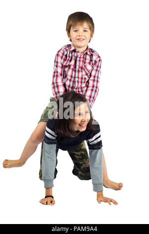 A young girl gives her little brother a horseback ride on a white background.  They are isolated with a clipping path.  Both kids are wearing camoufla Stock Photo