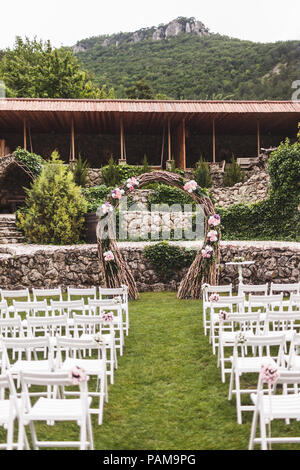 Cozy rustic wedding ceremony with flower arch and wooden white chairs on villa with mountain view Stock Photo