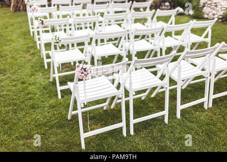 Cozy rustic wedding ceremony with wooden white chairs on green grass Stock Photo