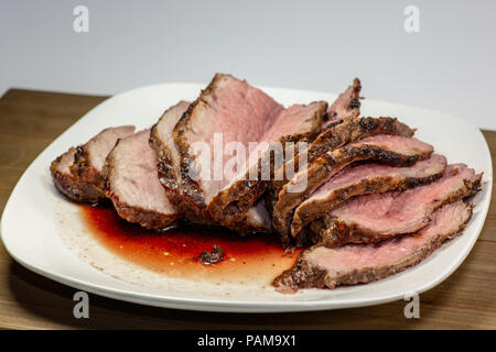 Grilled tri tip steak sliced on a white plate on the kitchen table Stock Photo
