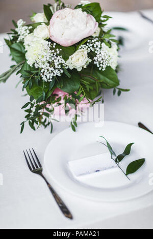 White wedding table decorated with green flowers arrangement, name cards, pink peony, white cutlery, rustic style Stock Photo