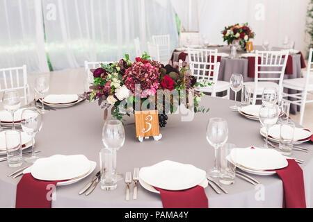 Wedding table, decorated with red flowers bouquets, candles, grey tablecloth, and white plates Stock Photo