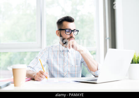 Portrait of handsome bearded businessman working at desk in office thoughtfully looking at laptop screen, copy space Stock Photo