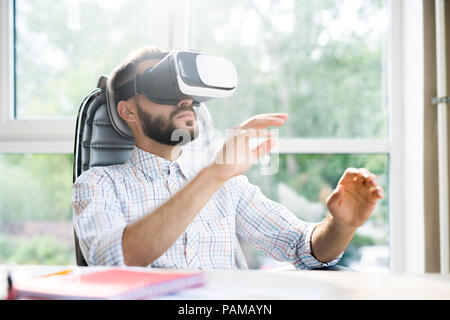 Portrait of handsome bearded man sitting at desk in office and enjoying VR simulator against window in sunlight, copy space Stock Photo