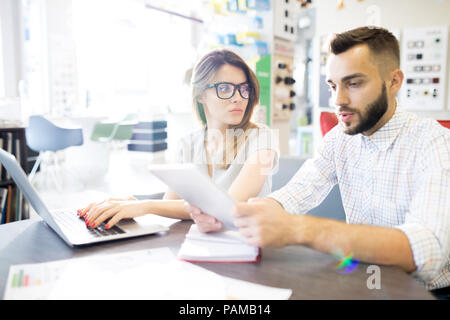 Portrait of two young managers, man and woman, sitting at desk in sunlit store and planning work, copy space Stock Photo