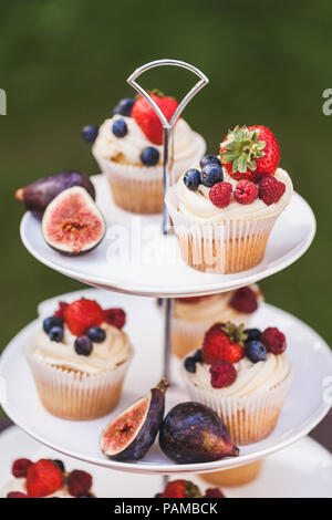 Fresh tasty cupcakes with berries on wedding reception table, decorated in red colour with flowers Stock Photo