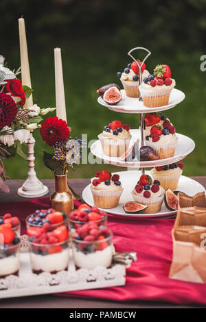 Fresh tasty cupcakes with berries on wedding reception table, decorated in red colour with flowers Stock Photo
