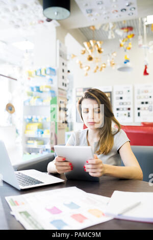 Portrait of beautiful young woman using digital tablet while sitting at desk in shop waiting for clients, copy space Stock Photo
