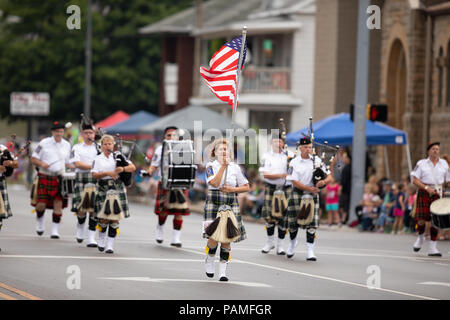 Peru, Indiana, USA - July 21, 2018 Woman carries the American flag leading the Indianapolis 500 Gordon Pipers Horse Shoe Pipes and Drums group of bagp Stock Photo