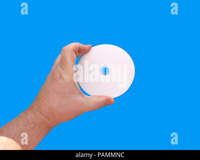 A hand holding a white/blank CD or DVD media against a blue background Stock Photo