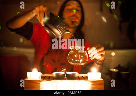 Man serving oolong tea from a chinese teapot into a glass pitcher as part of a candle lit Gong Fu Cha tea ceremony Stock Photo