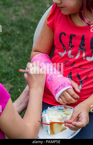 Photo of young girl and right arm is in pink cast., having friend sign it. Model Release #114 Stock Photo