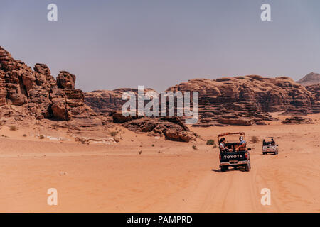 pickup tricks full of tourists drive in a convoy across the red desert sands in the famous Wadi Rum National Park, Jordan Stock Photo