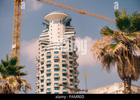 the Isrotel hotel tower building with a crane and palm trees in the foreground in Tel Aviv, Israel Stock Photo