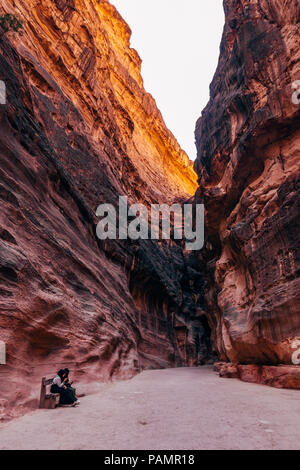 two muslim girls rest and use their phones on the path into Petra, Jordan Stock Photo