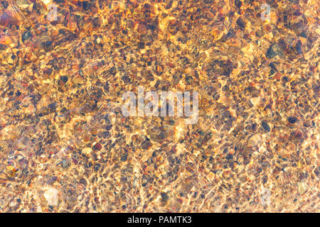 Rocks on the sandy bottom of the sea ripples through small waves on a sunny day Stock Photo