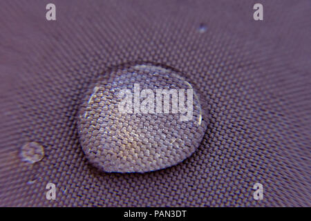 Water drops on a waterproof surface showing the details of the fabric through the transparent drop. Stock Photo