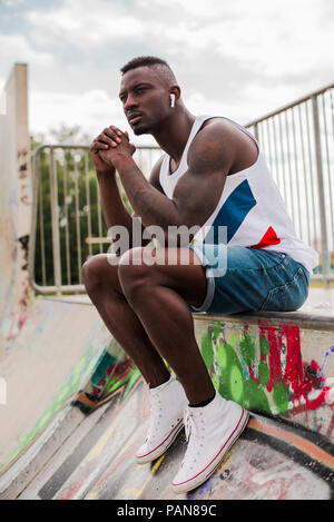 Young man in skatepark sitting on wall, listening music Stock Photo