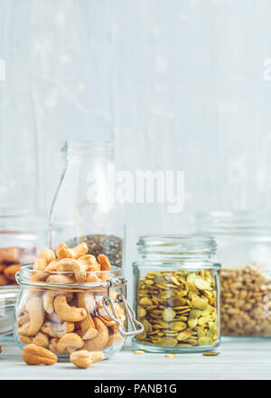 Various nuts and seeds in glass jars over white wooden table against white background. The concept of vegetarian and organic food. Stock Photo