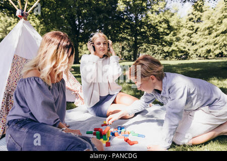 Two young women and a boy playing with building blocks in a park Stock Photo