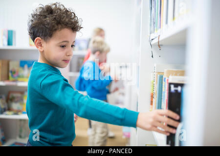 Schoolboy taking book from shelf in school library Stock Photo