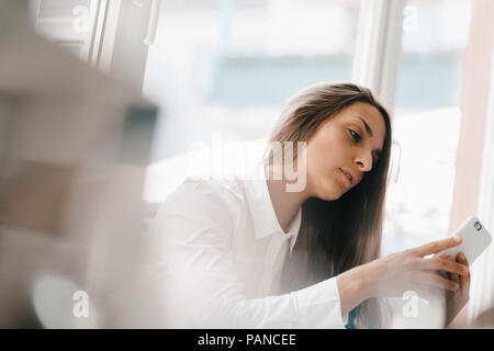 Young businesswoman sitting at window, using smartphone Stock Photo