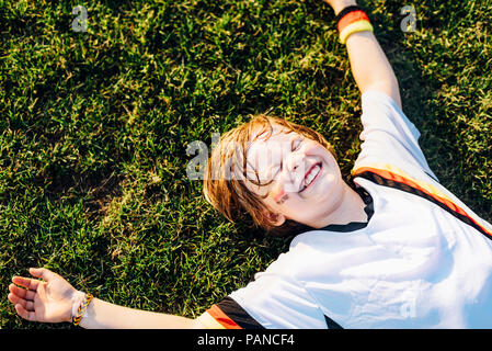 Boy in German soccer shirt lying on grass, laughimg Stock Photo