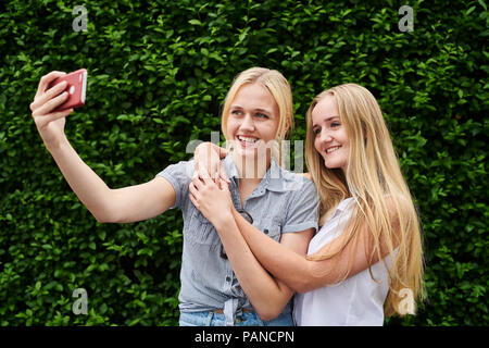 Two happy young women taking a selfie at a hedge Stock Photo