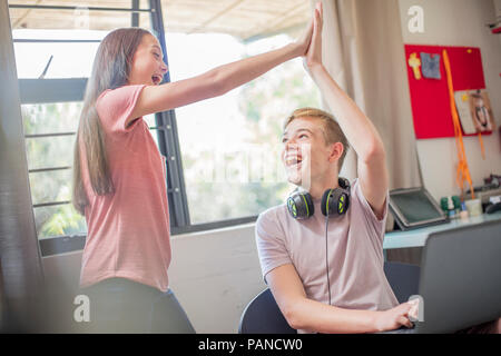 Happy teenage girl and boy with laptop high fiving Stock Photo