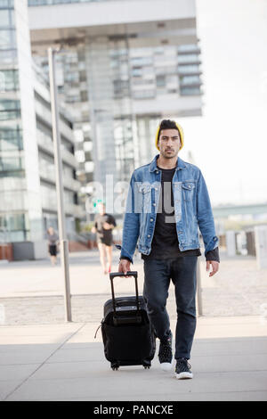 Germany, Cologne, portrait of young man pulling trolley Stock Photo
