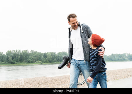 Happy father and son walking with unicycle at the riverside Stock Photo