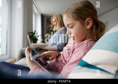 Mother and daughter at home sitting on couch using laptop and tablet Stock Photo