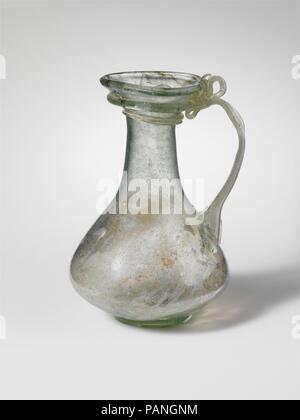 Glass jug. Culture: Roman. Dimensions: H.: 4 1/8 in. (10.5 cm)  Diam.: 1 5/8 x 2 13/16 x 1 1/2 in. (4.1 x 7.1 x 3.8 cm). Date: 3rd-4th century A.D..  Small jug.  Translucent light blue green; handle, foot ring, and trail in same color.  Uneven rim folded over and into flaring mouth; cylindrical neck, expanding downwards; biconical body; low, applied foot ring; flat bottom, with pontil scar; three-ribbed strap handle, attached to upper body with long downward claws, drawn up, round, and in, folded down and up, and attached to underside of mouth and edge of rim over trail, with projecting hollow Stock Photo