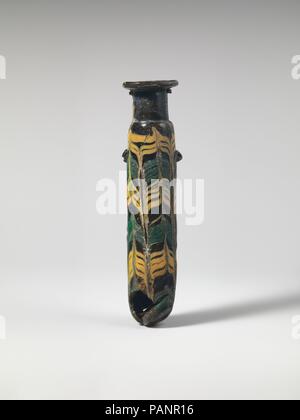 Glass alabastron (perfume bottle). Culture: Greek, Eastern Mediterranean. Dimensions: H.: 4 7/8 in. (12.4 cm). Date: late 4th-early 3rd century B.C..  Translucent pale yellowish green with darker blue green streaks, with handles in same color; trails in opaque yellow and opaque turquoise blue.  Horizontal rim-disk; tall cylindrical, slanting neck; small sloping shoulder; straight-sided cylindrical body, with slight upward taper; convex bottom but with off-center pointed tip; on body, two lug handles, applied over trail pattern; one with a tooled upward horizontal indent, the other with a sidew Stock Photo