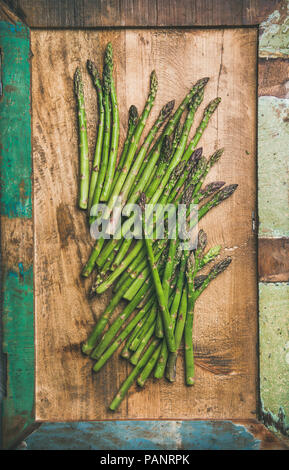 Raw uncooked green asparagus over rustic wooden tray background Stock Photo
