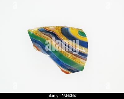 Glass striped mosaic bowl fragment. Culture: Roman. Dimensions: 1 5/8 × 2 1/8 × 1/8 in. (4.2 × 5.4 × 0.3 cm)  Estimated diameter 5 1/8 in. (13 cm). Date: late 1st century B.C.-early 1st century A.D..  Rim and side of a shallow hemispherical bowl.  Translucent cobalt blue, purple appearing semi-opaque brick red, light blue appearing green, opaque yellow and white, and colorless.  Vertical rim with beveled inner lip; convex curving side, turned in sharply towards bottom.  Striped pattern formed from lengths of different canes in parallel, diagonal lines: one cane in green; another in yellow outl Stock Photo
