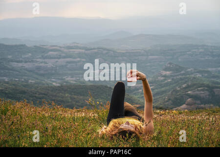 Spain, Barcelona, young woman lying on meadow on Montcau Mountain taking selfie Stock Photo