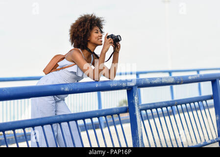 Smiling young woman standing on bridge taking pictures with camera Stock Photo