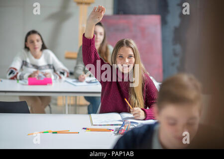 Happy teenage girl raising hand in class Stock Photo