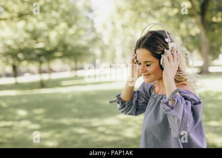 Smiling young woman in a park enjoying listening to music with headphones Stock Photo