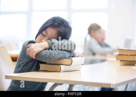 Schoolgirl sleeping on stack of books on table in school Stock Photo