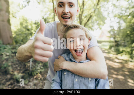 Portrait of happy young man embracing boy on forest path Stock Photo