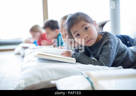 Portrait of schoolgirl lying on the floor with classmates reading book in school break room Stock Photo