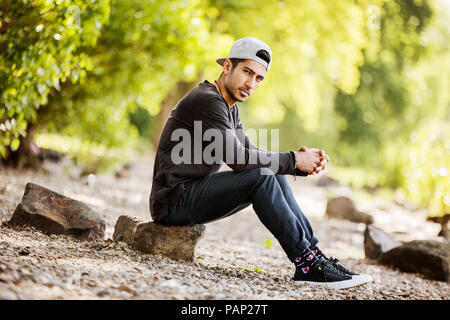 Portrait of young man with baseball cap sitting in nature Stock Photo